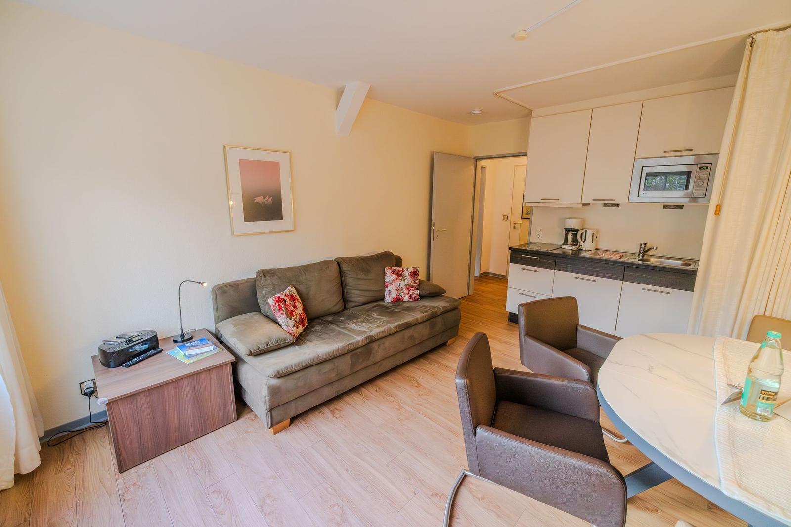 Wohnung mit Sofa, Essbereich und Küche. Holzboden und weiße Wände.