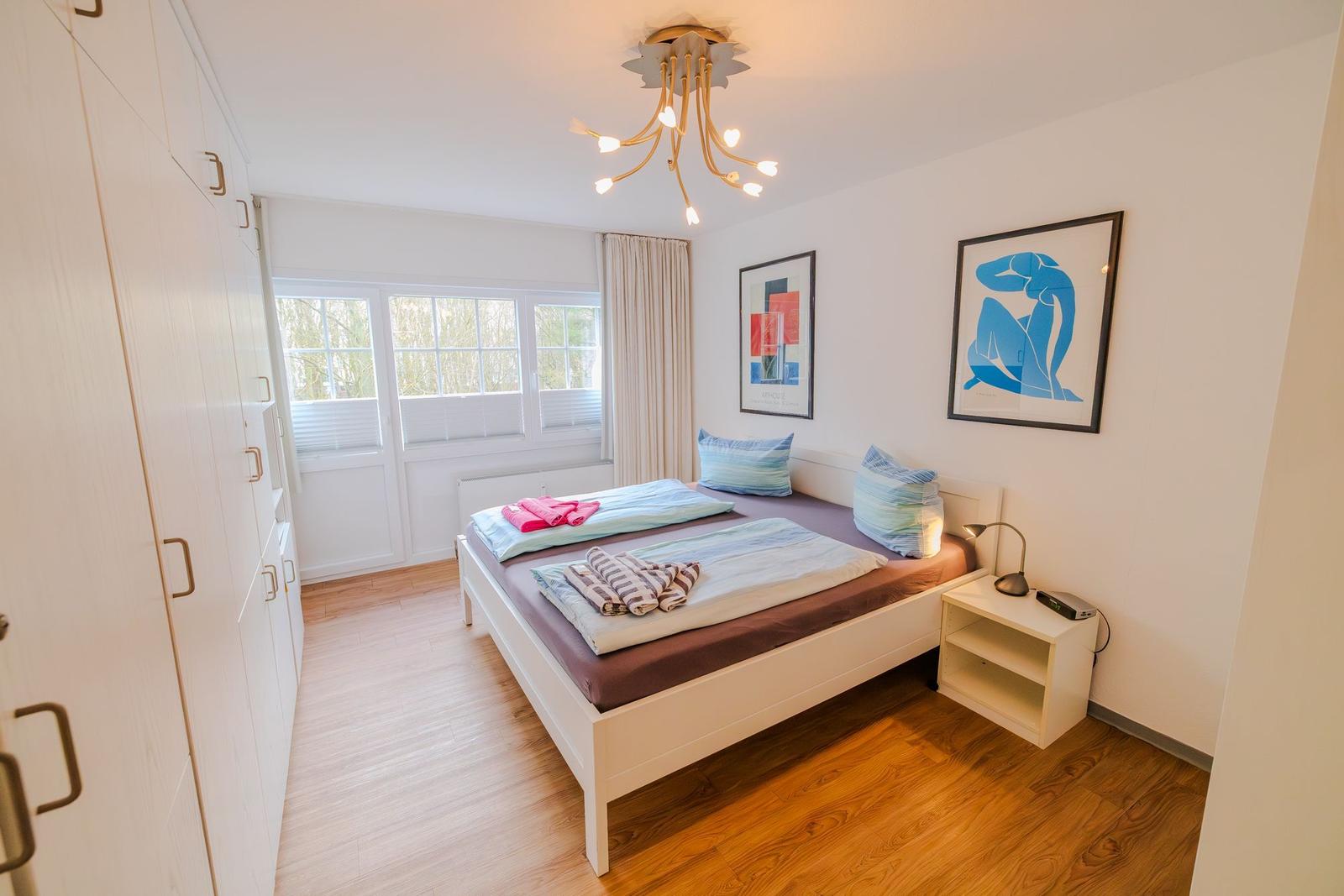 Schlafzimmer mit Bett, Kleiderschrank und Fenster. Wandbild und Nachttisch sind vorhanden.