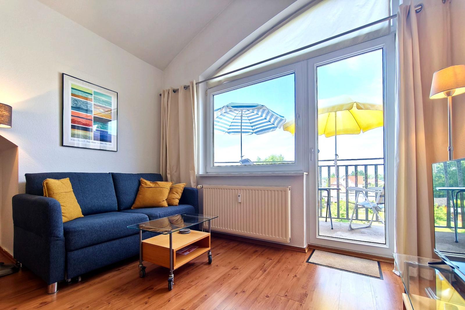 Lichtdurchfluteter Wohnbereich mit blauer Couch und Zugang zum Balkon
