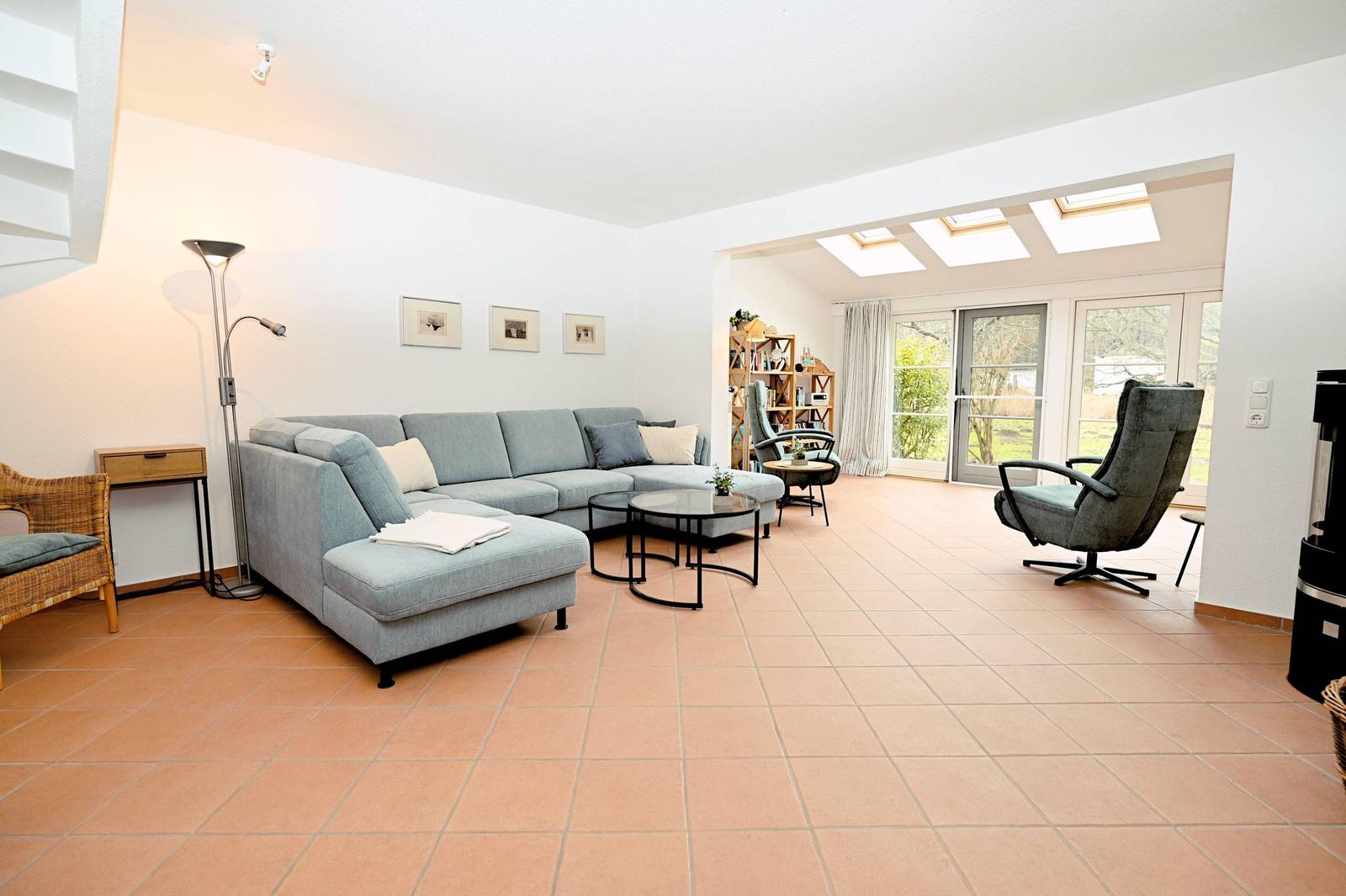 Wohnzimmer mit Sofa, Sessel und Terrassentür. Terrasse mit Blick auf Grünfläche.