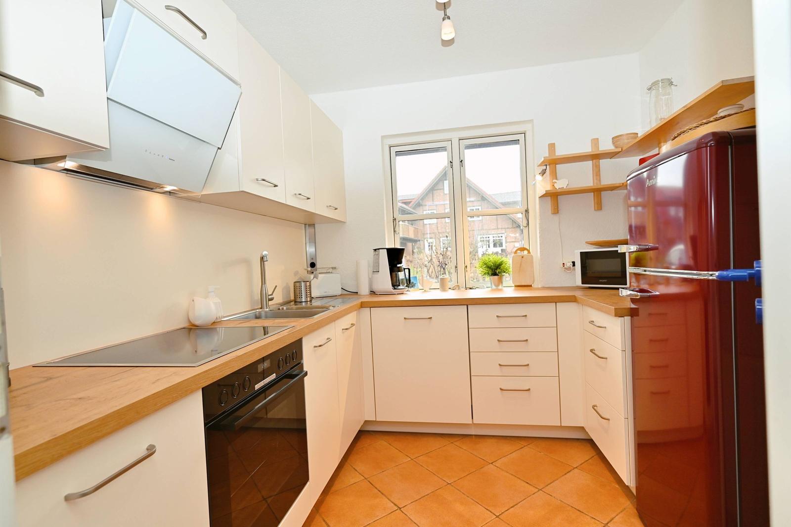 Küche mit weißen Schränken, Holz Arbeitsplatte und rotem Kühlschrank.