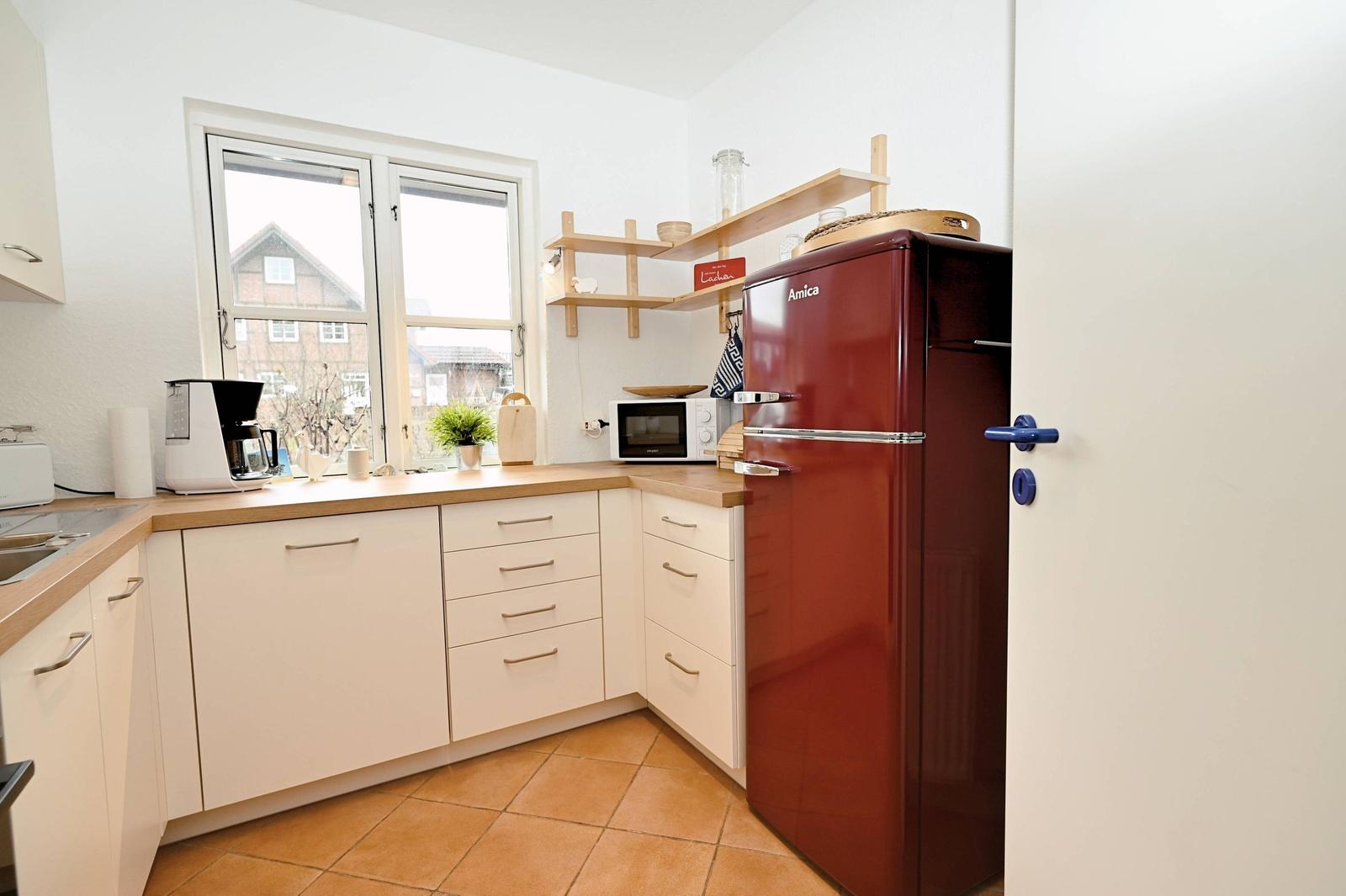 Küche mit rotem Kühlschrank, Holzregalen und Fensterblick auf Dächer.
