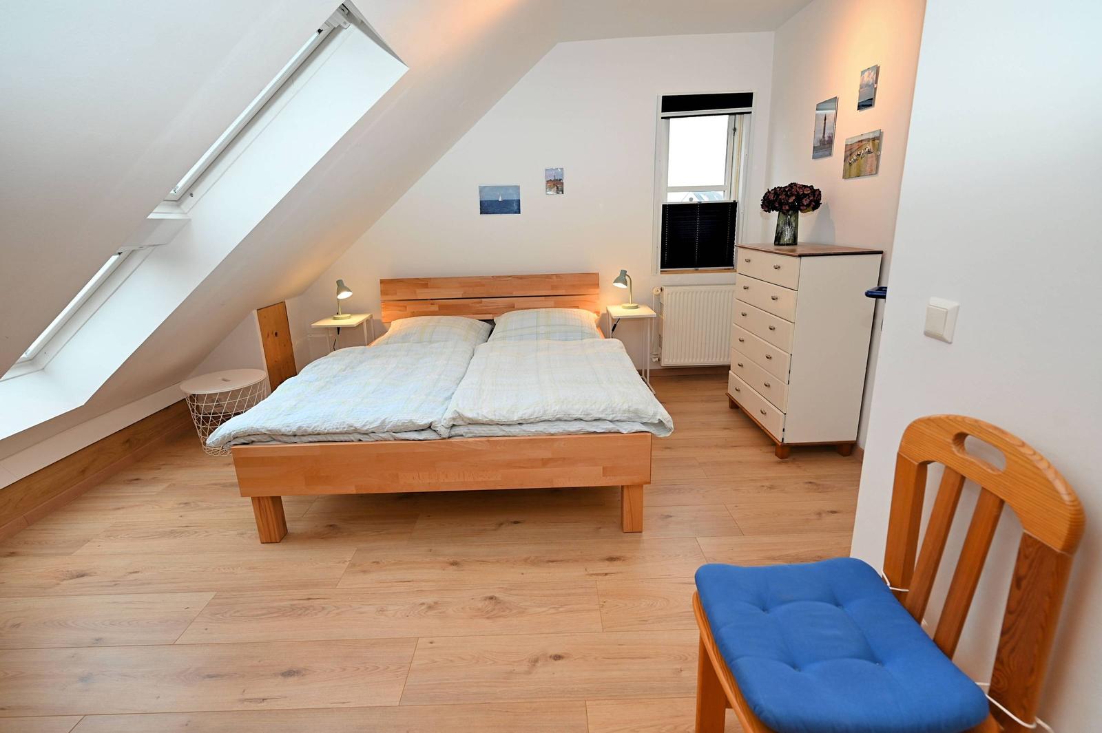 Schlafzimmer mit Dachschrägen, Doppelbett, Schrank und Sessel mit blauem Sitzkissen.