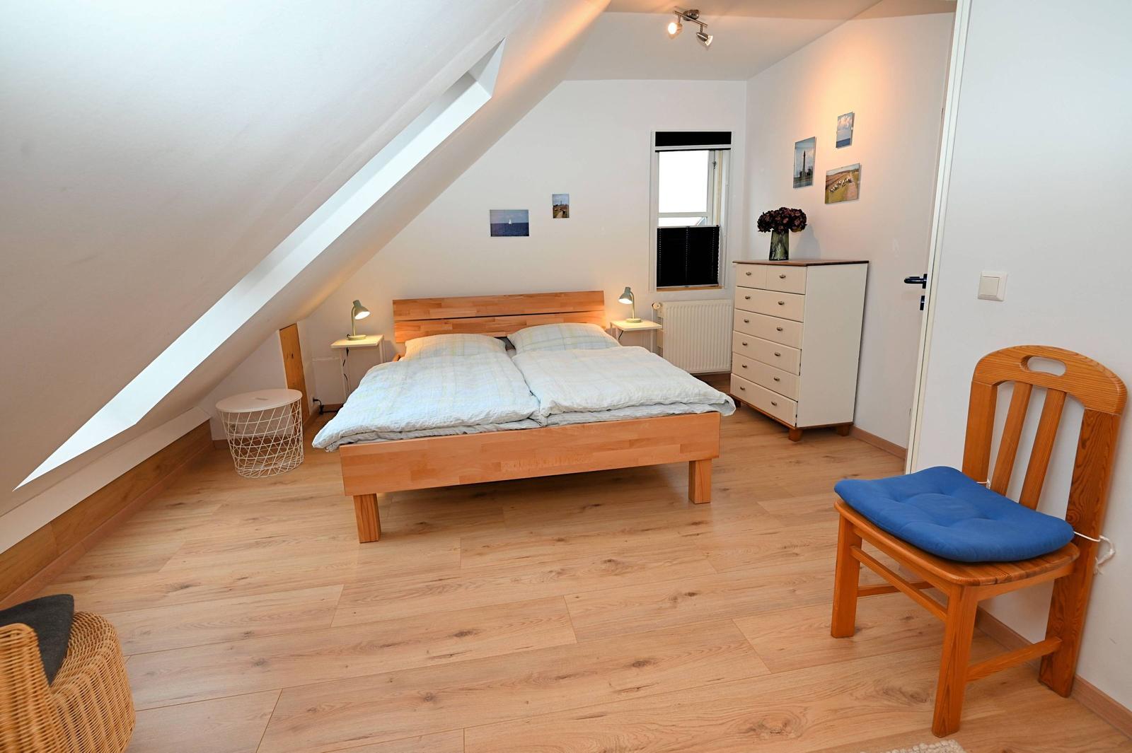 Schlafzimmer mit Dachschrägen, Holzboden und Doppelbett. Holzstuhl mit blauer Sitzfläche.