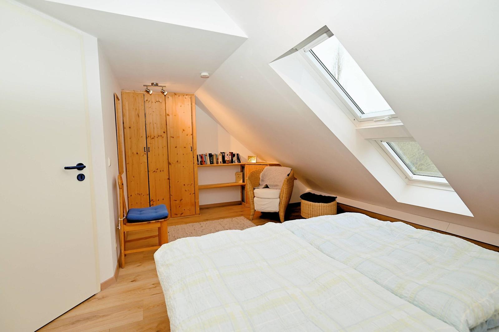 Schlafzimmer mit Dachschrägen, Dachfenster, Holzschränken und Bett.
