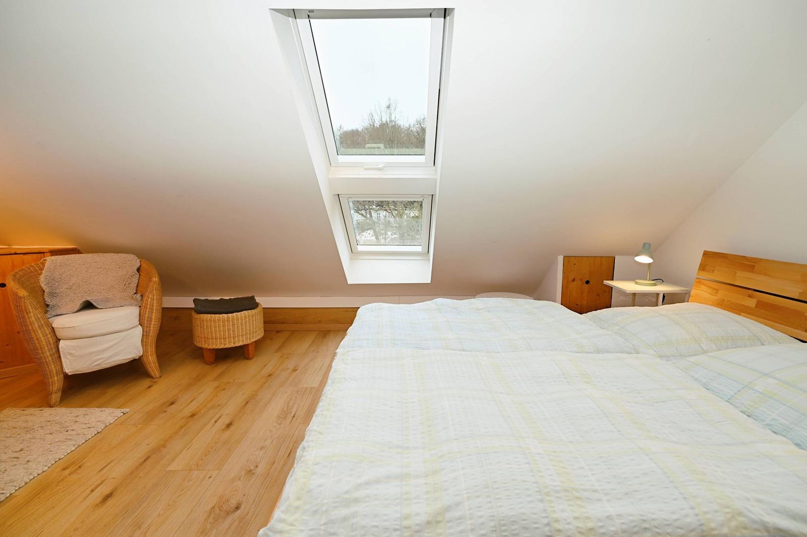 Schlafzimmer mit Dachfenster, Bett, Stuhl und Nachttisch.