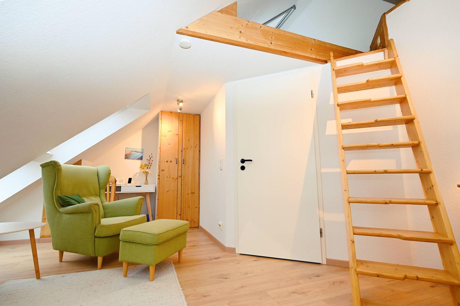 Dachgeschosszimmer mit grüner Sitzgruppe, Holztreppe und Kleiderschrank.
