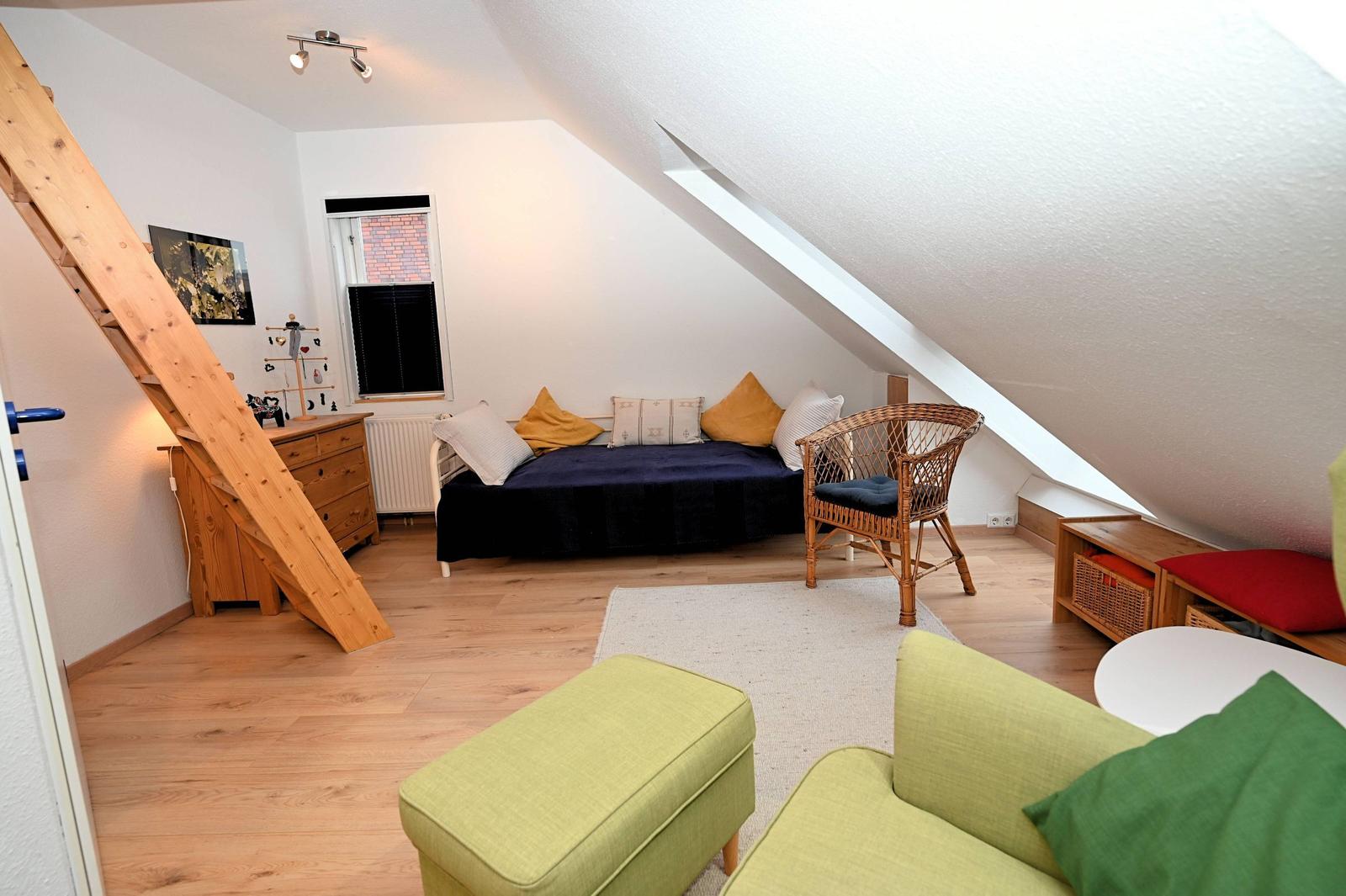 Schlafzimmer mit Dachschrägen, Bett, Stuhl und Holzboden.