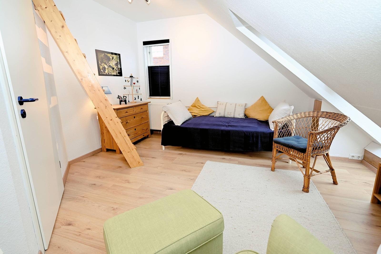 Ein Schlafzimmer mit Dachschräge, Bett, Stuhl und Holzfußboden.