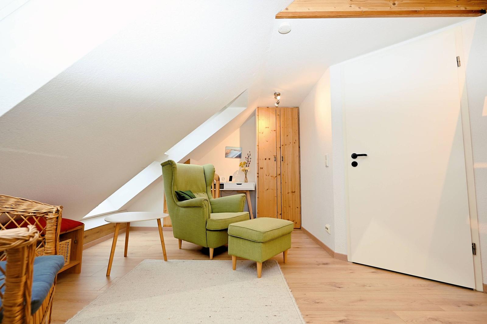 Dachgeschosszimmer mit grünem Sessel, Holzboden und schräger Decke.
