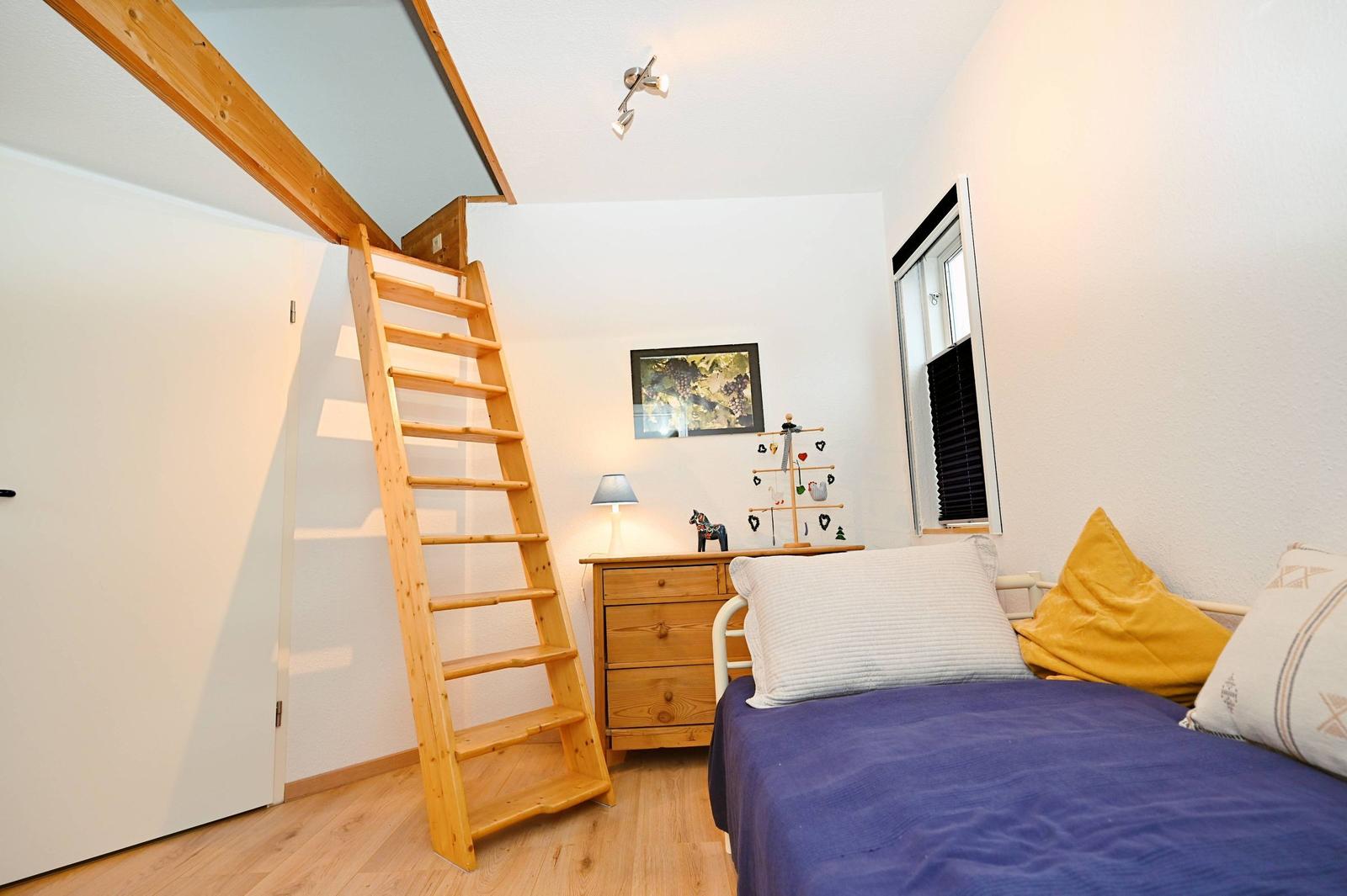 Schlafzimmer mit Holztreppe, Bett, Nachttisch und Fenster.