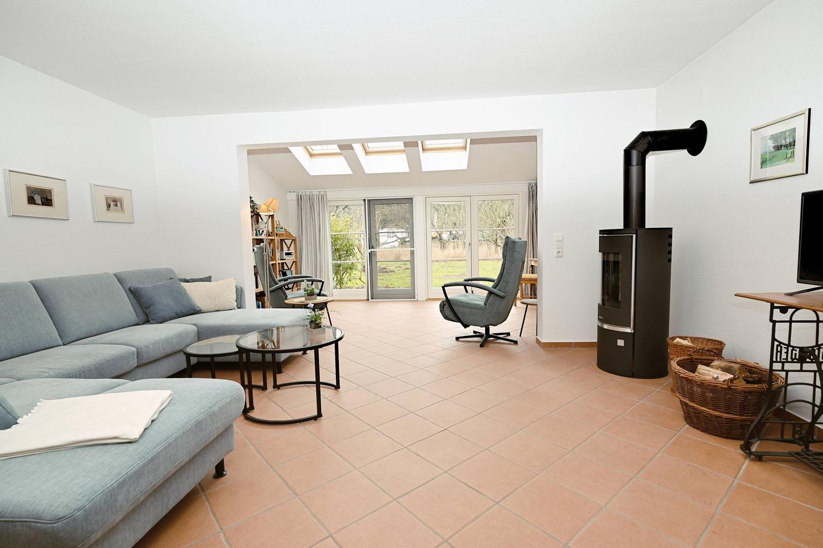 Wohnzimmer mit Sofa, Sessel und Kaminofen. Durchgang zu Terrasse mit Türen und Dachfenstern.