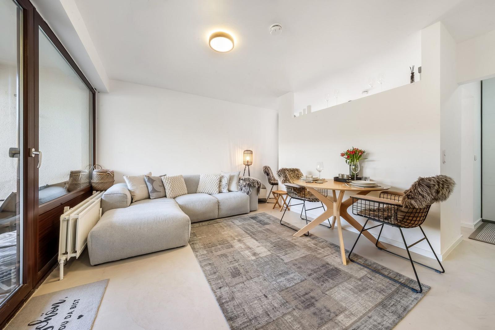 Living and dining area with sofa, table and chairs. Glass door leads to balcony.