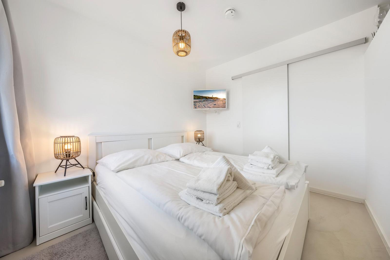 Bedroom with white bed, nightstand, lamp, and closet.