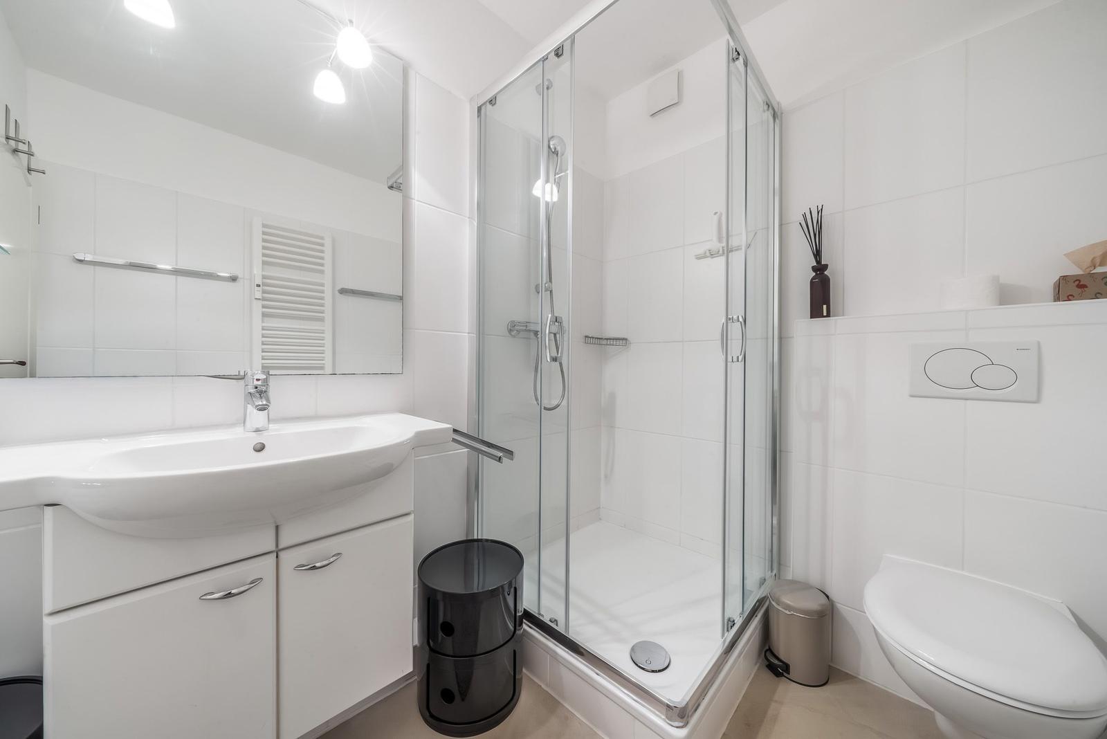 Bathroom with shower, sink, and toilet. White tiles and modern fixtures.