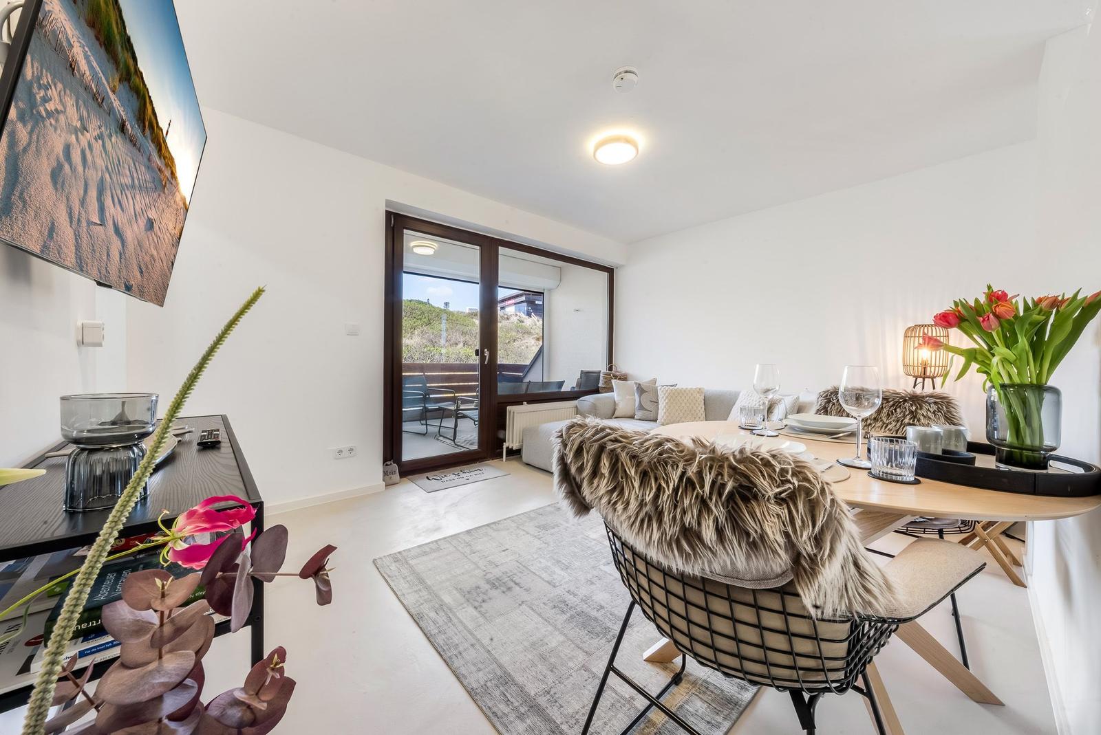Living and dining area with table, chairs, and view of balcony.