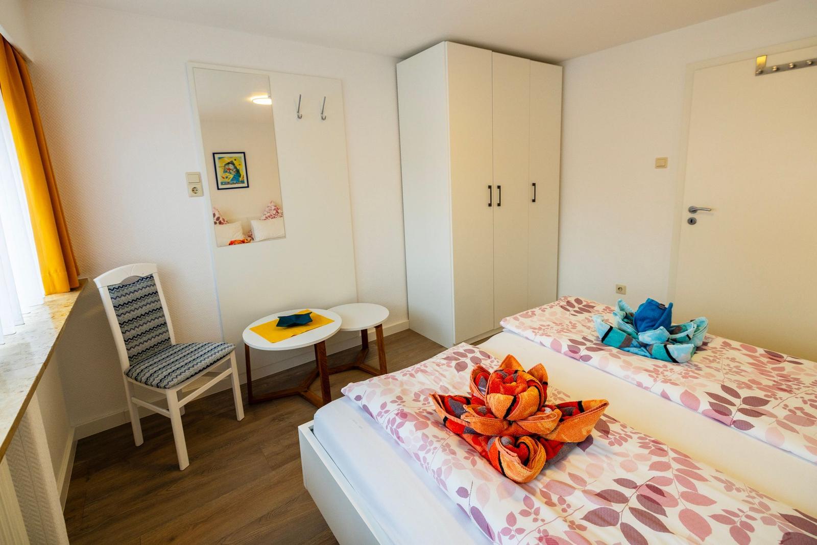 Zimmer mit zwei Betten, Kleiderschrank, Stuhl und Spiegel an der Wand.