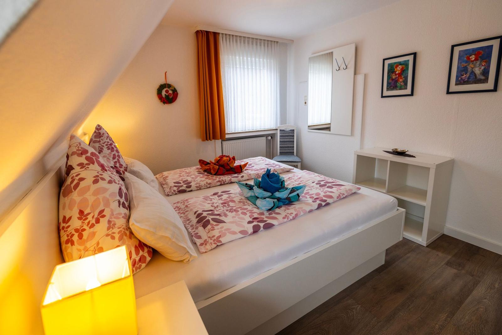 Schlafzimmer mit Bett, Fenster, Spiegel und Schrank. Decke geneigt, Holzboden.