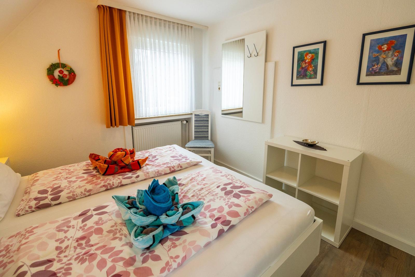 Schlafzimmer mit Bett, Fenster, Spiegel und Schrank. Auf dem Bett liegen gefaltete Handtücher.