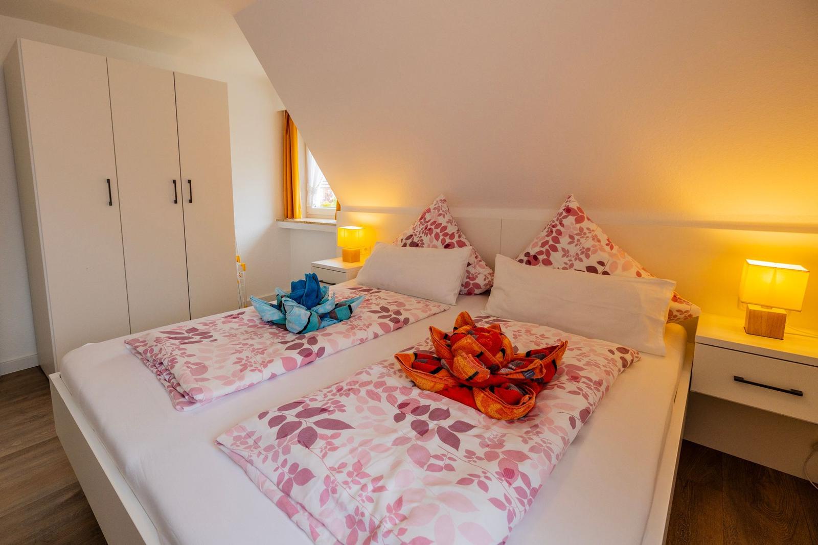 Schlafzimmer mit Doppelbett, Nachttischen und Kleiderschrank. Auf dem Bett liegen gefaltete Handtücher.
