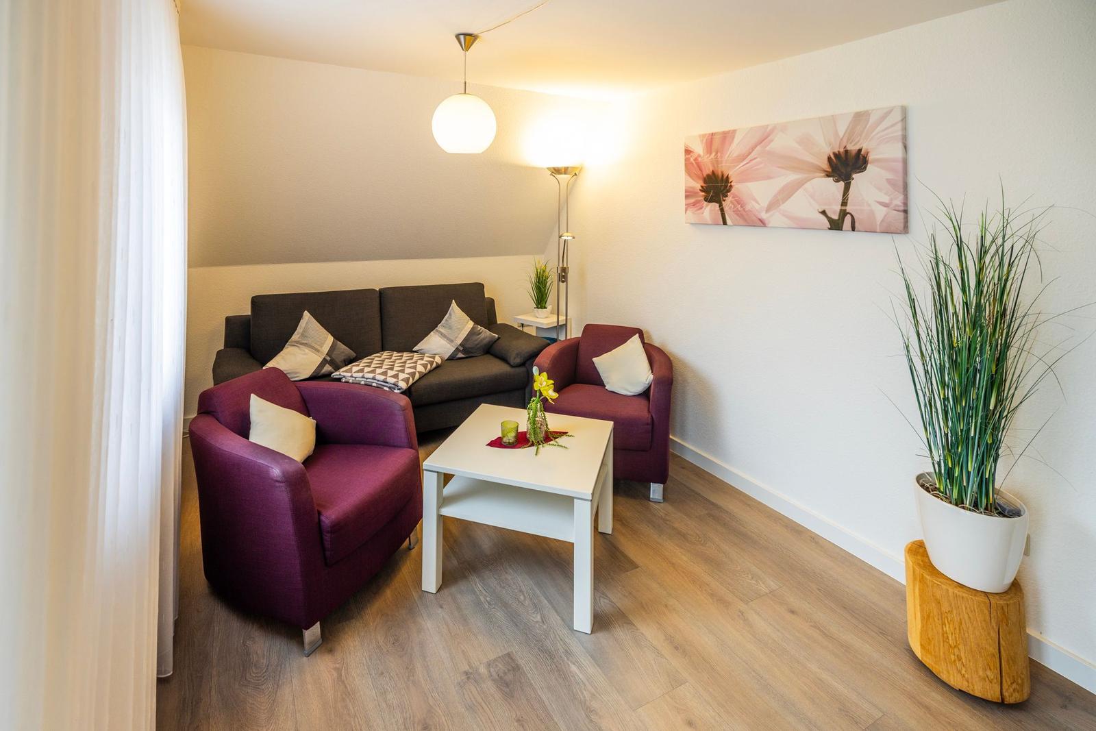 Wohnzimmer mit Sofa, zwei Sesseln, Tisch und Pflanze.