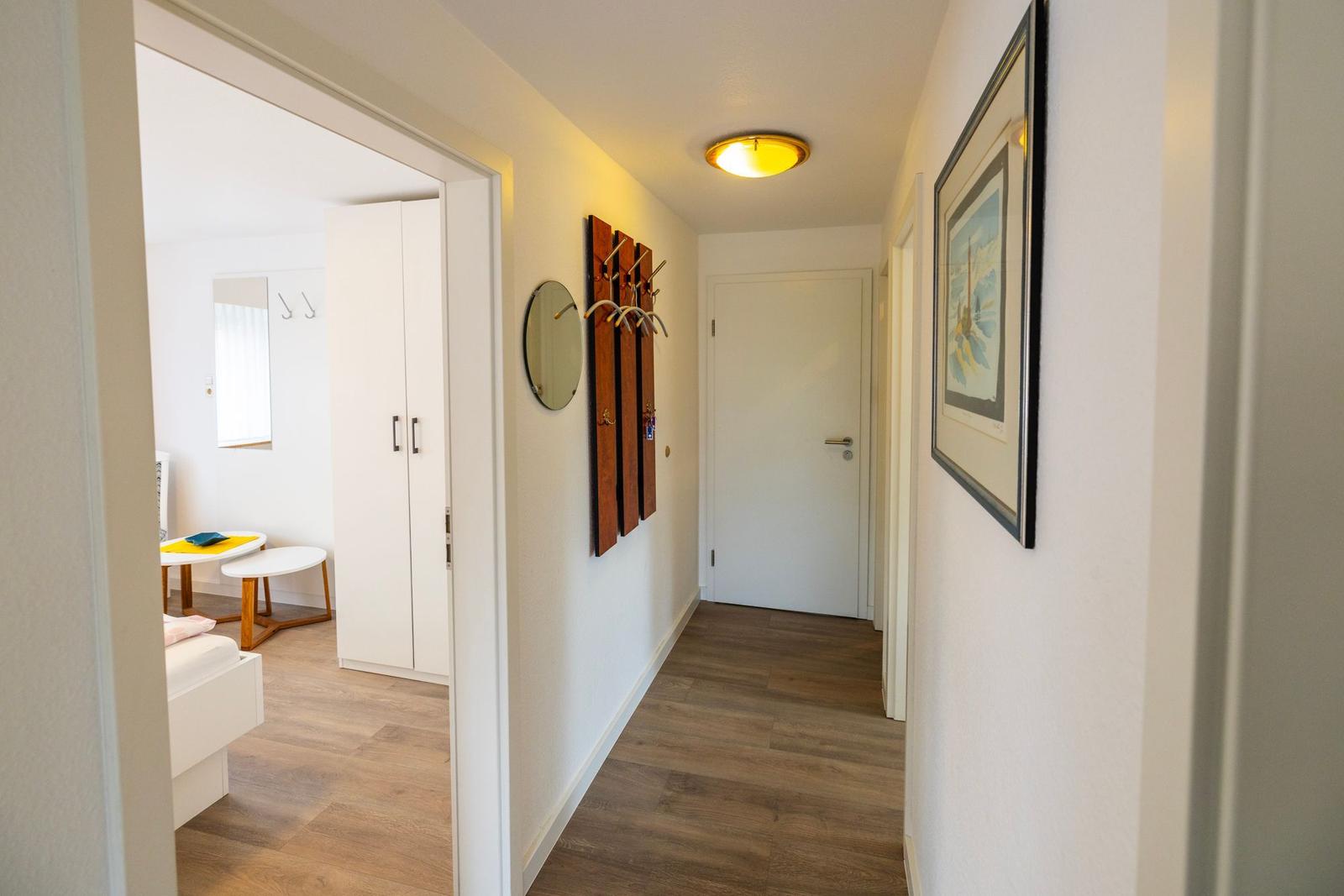 Flur mit Holzboden, Wandbild und Garderobe. Durchgang zu Schlafzimmer mit Schrank und Tisch.