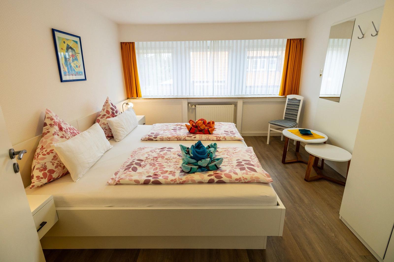 Schlafzimmer mit Doppelbett, Fenster, Stuhl und Tisch.