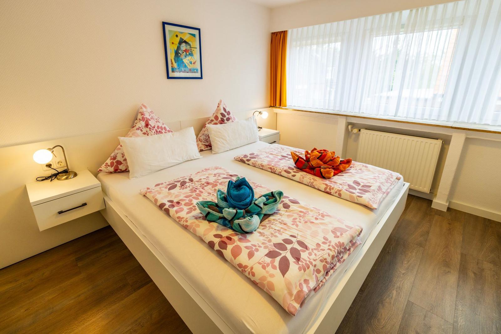 Schlafzimmer mit Doppelbett, Fenster und Nachttisch mit Lampe.