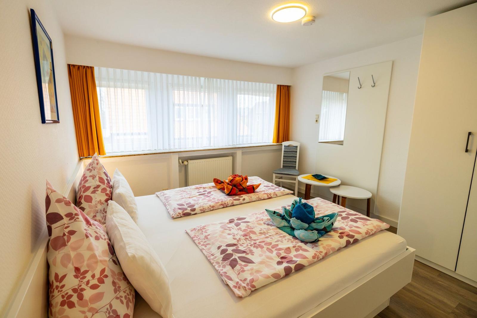 Ein Schlafzimmer mit Doppelbett, Fenster, Spiegel und Kleiderschrank.