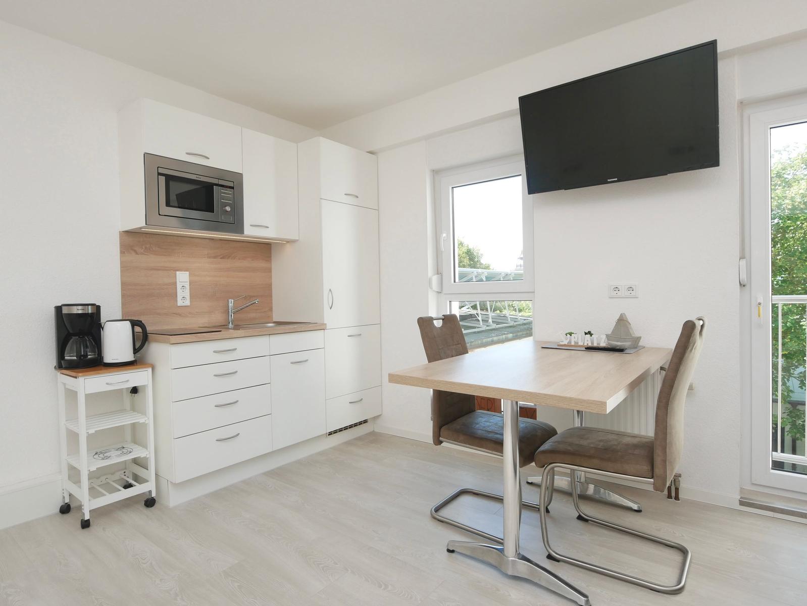 Küche mit Esstisch, TV und Balkontür. Moderne Einrichtung mit Holz- und Metallmöbeln.