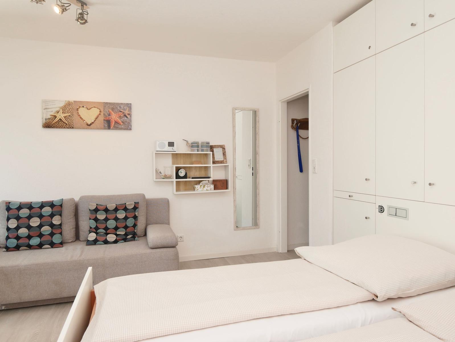 Schlafzimmer mit Bett, Sofa, Kleiderschrank und Wandregal.