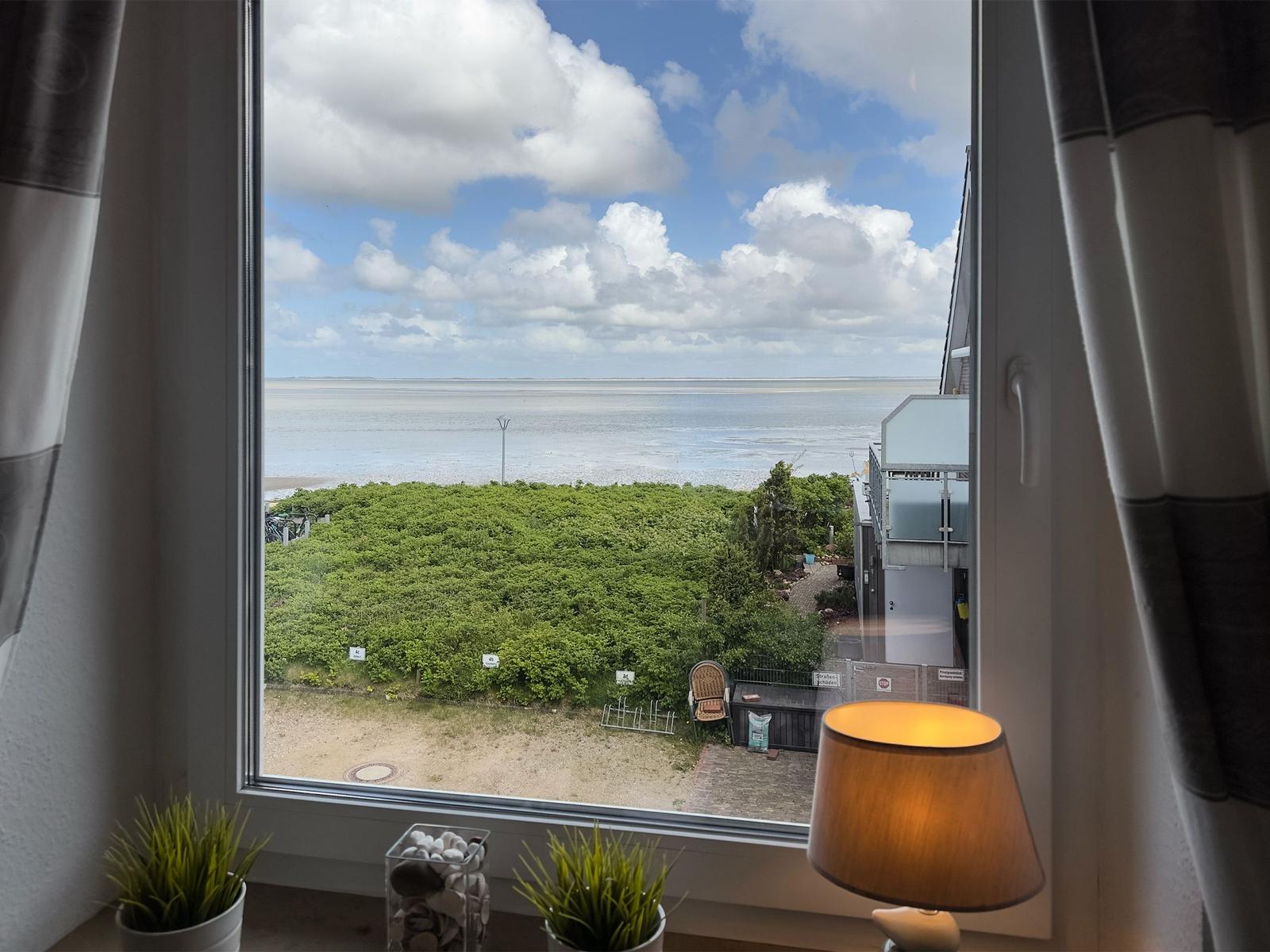 View from the window to beach and sea under blue sky with white clouds.