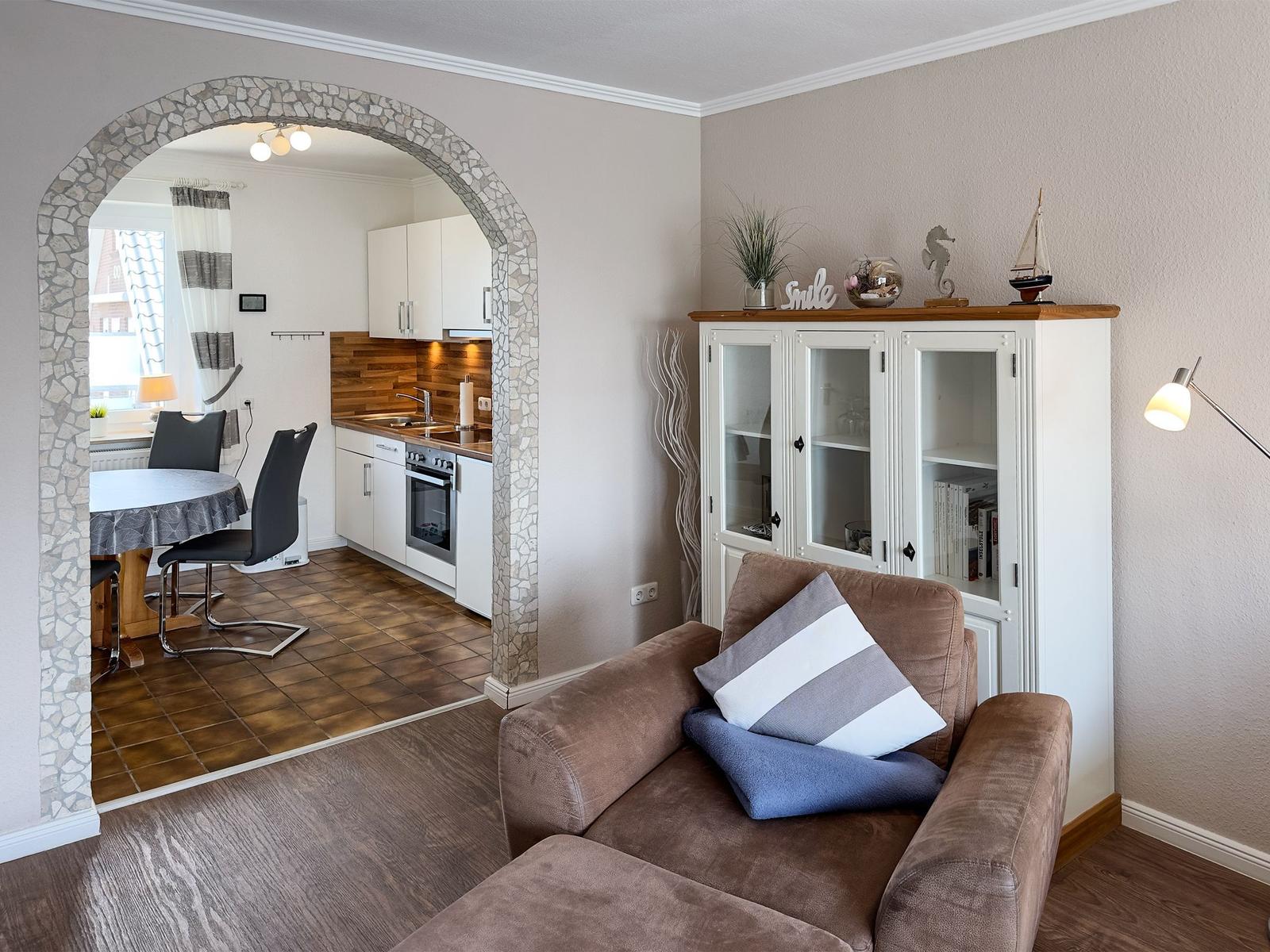 Living room with sofa and glass cabinet. Kitchen with table and chairs in the background.