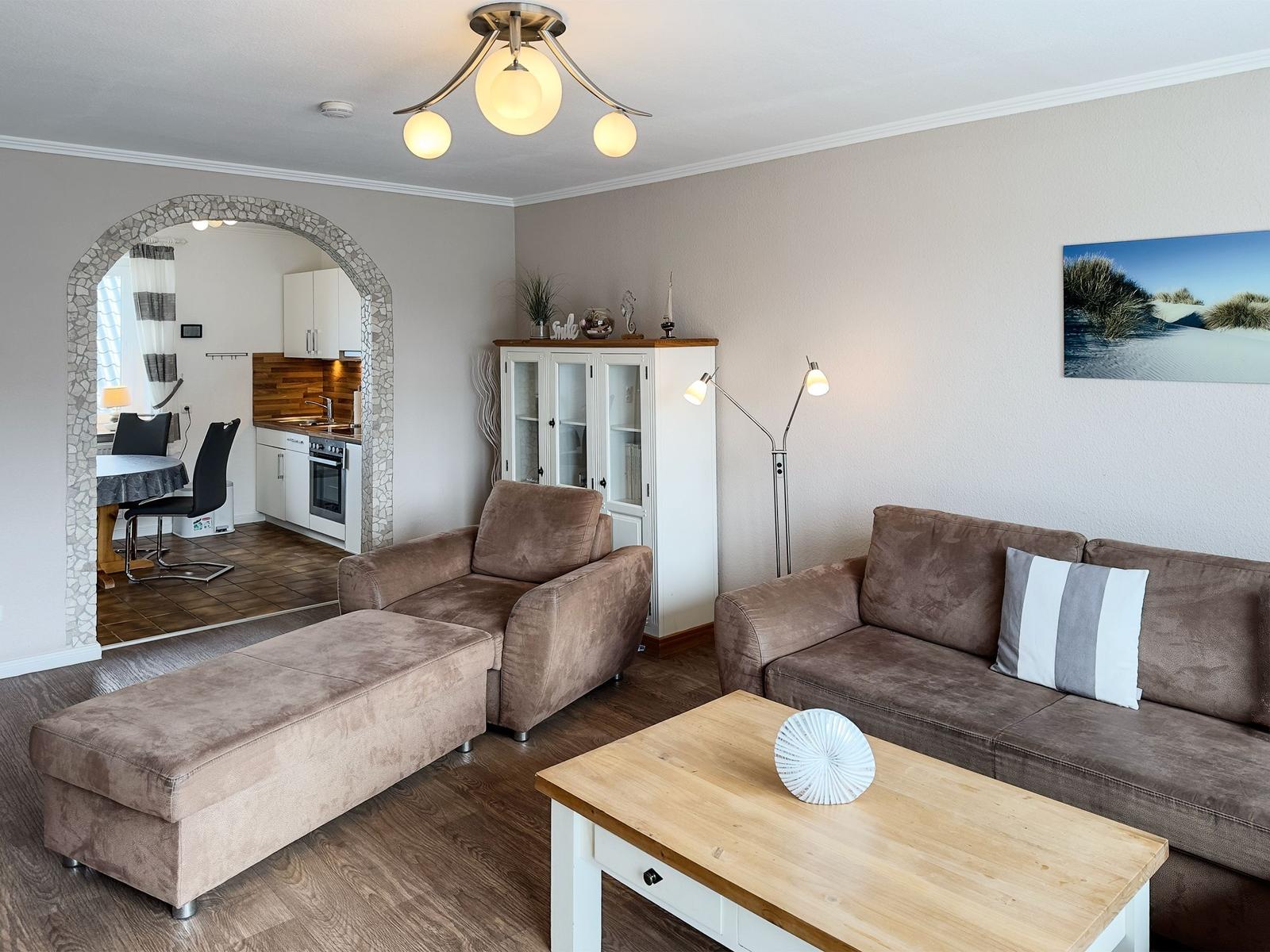 Living room with sofa, armchair, and kitchen area in background.
