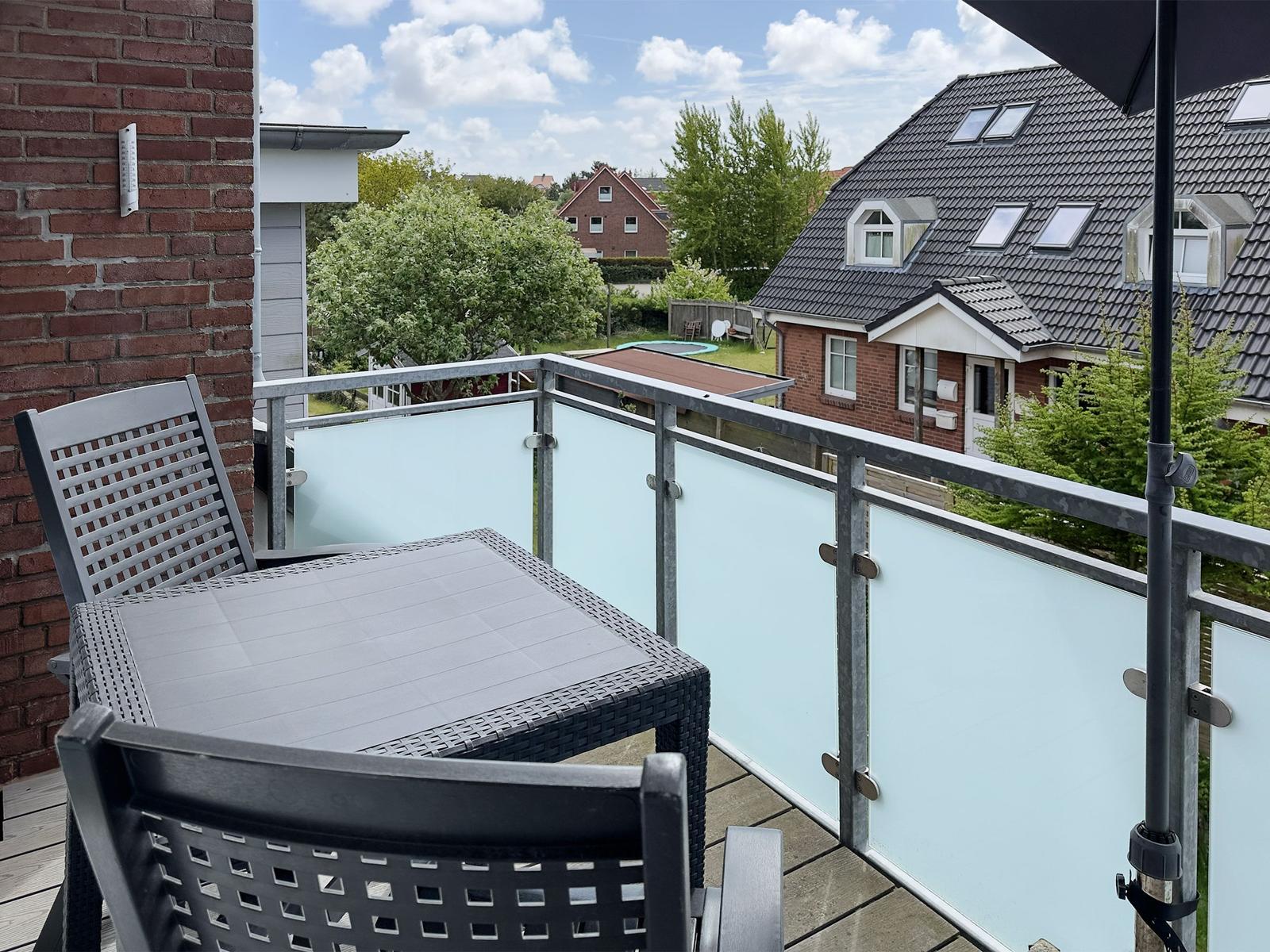 Balcony with table and chairs, view of houses and trees.