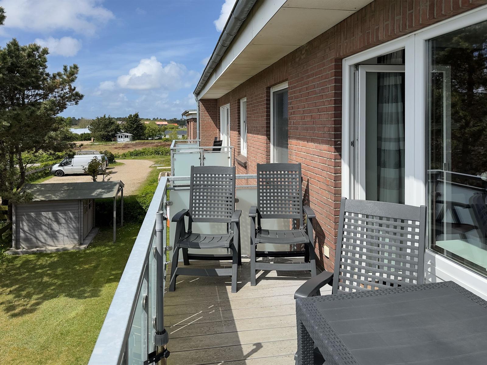 Terrace with three chairs and table, view of green area and buildings.