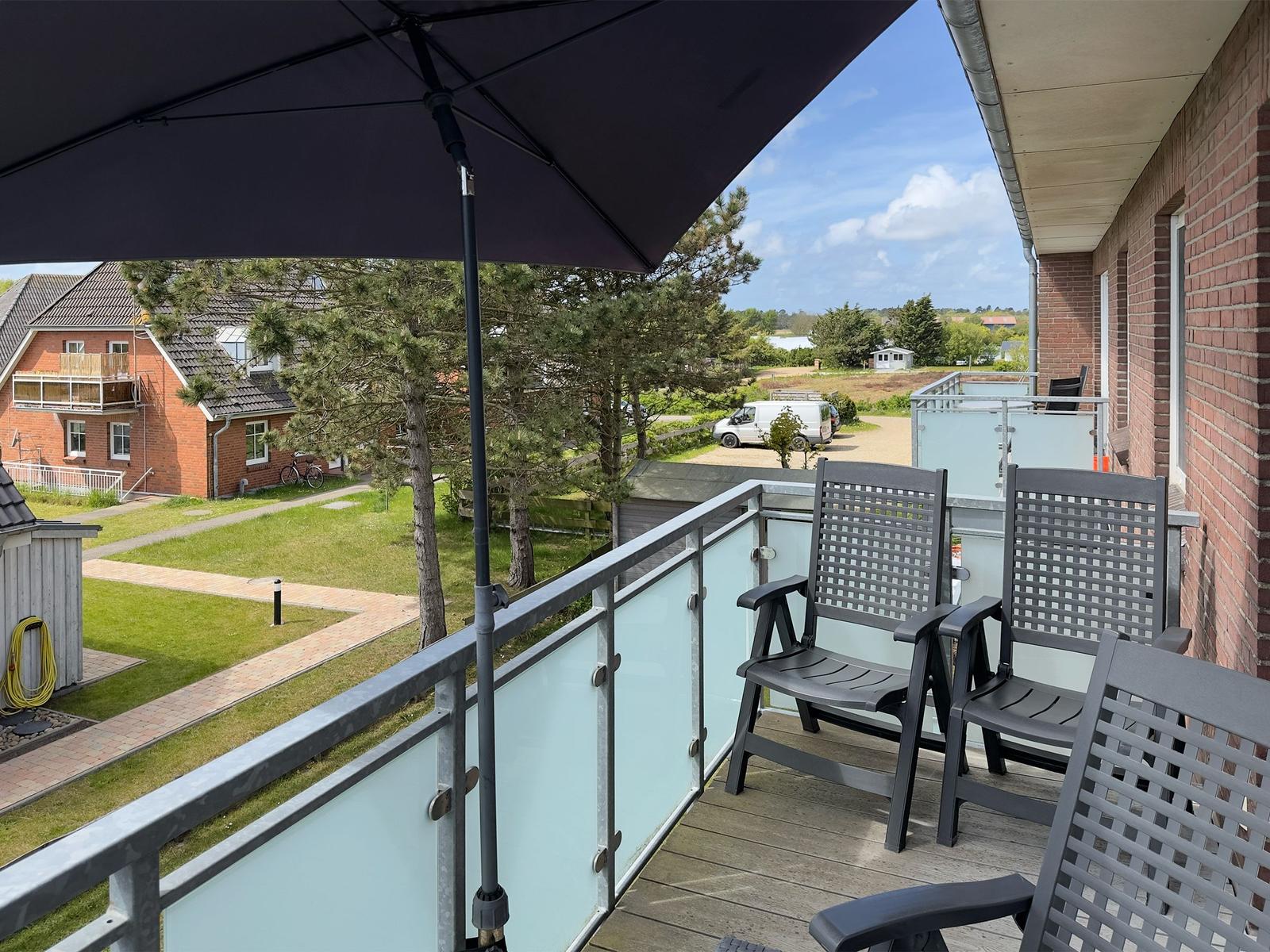Terrace with umbrella and chairs, view of lawns and buildings.