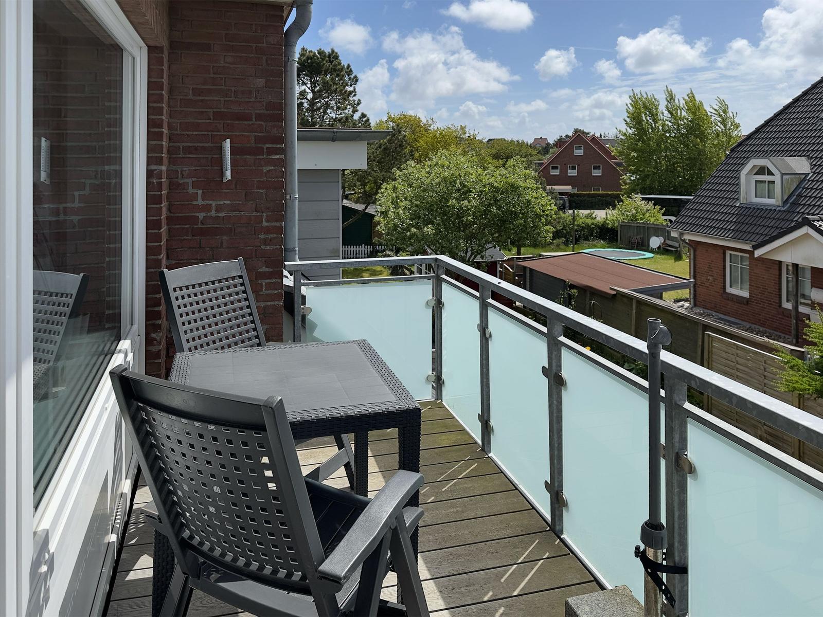 Terrace with table and chairs, glass railing, and view of garden and neighboring houses.
