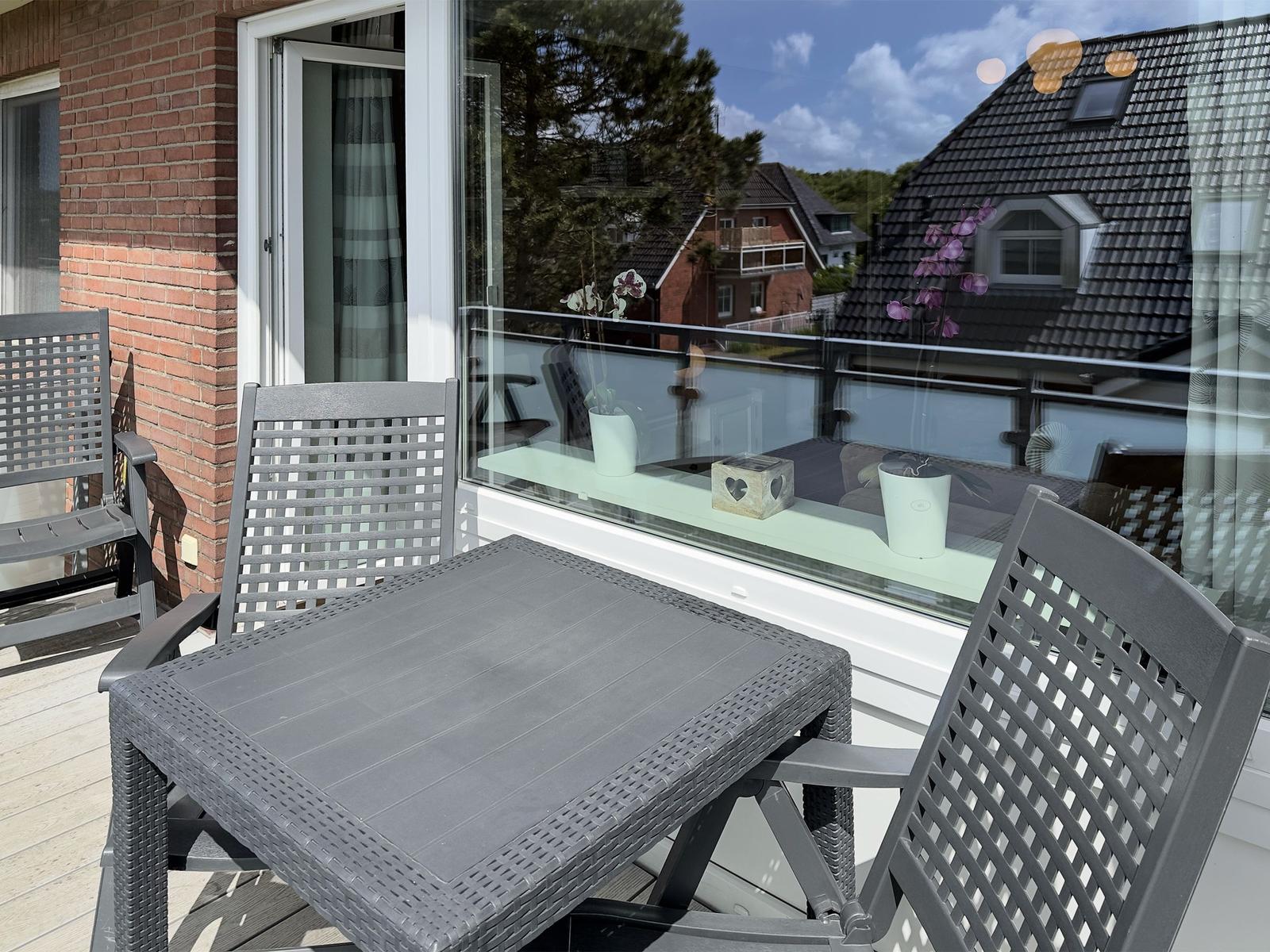 Terrace with gray table and chairs, glass railing, and view of rooftops.