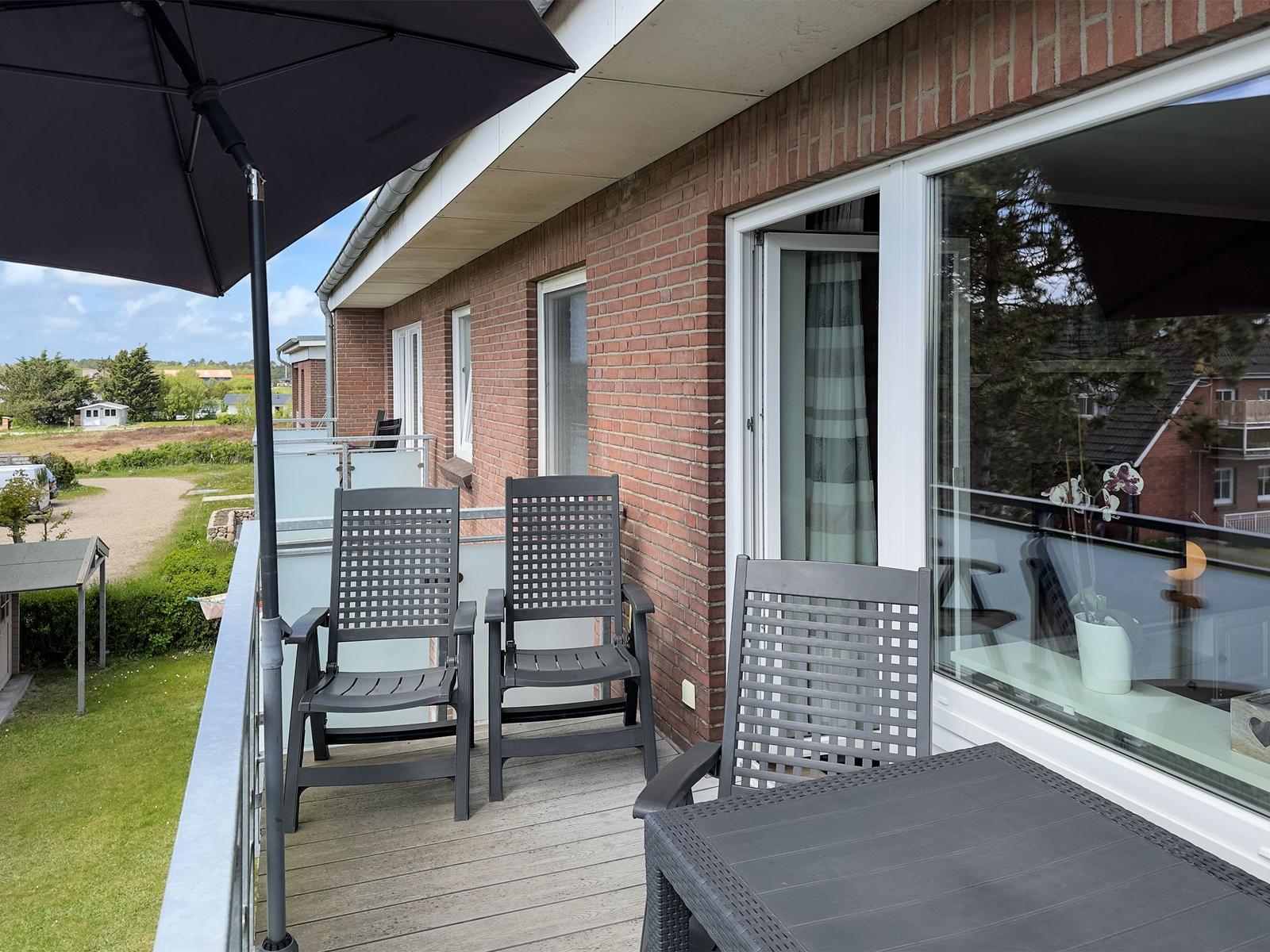 Terrace with table, three chairs, and umbrella. View of garden and neighboring houses.