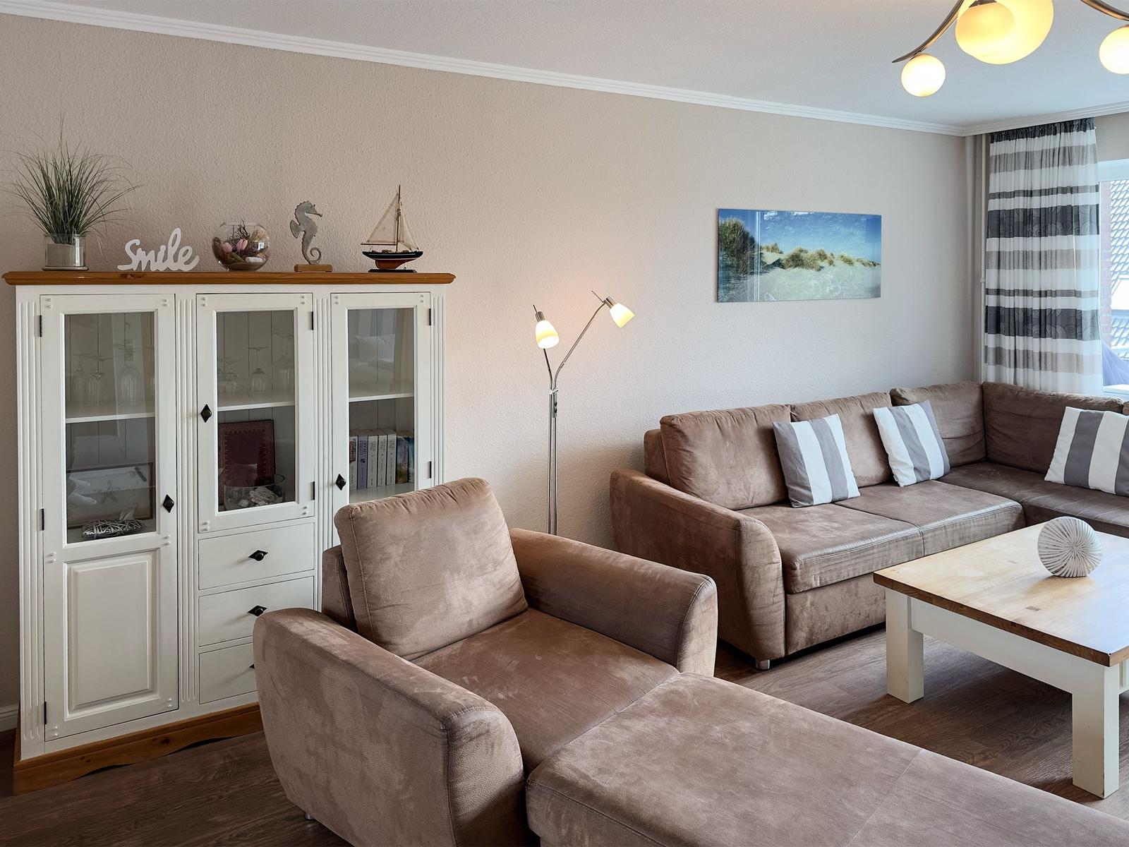 Living room with brown sofa, white sideboard, and table. Wall art and lamp are visible.