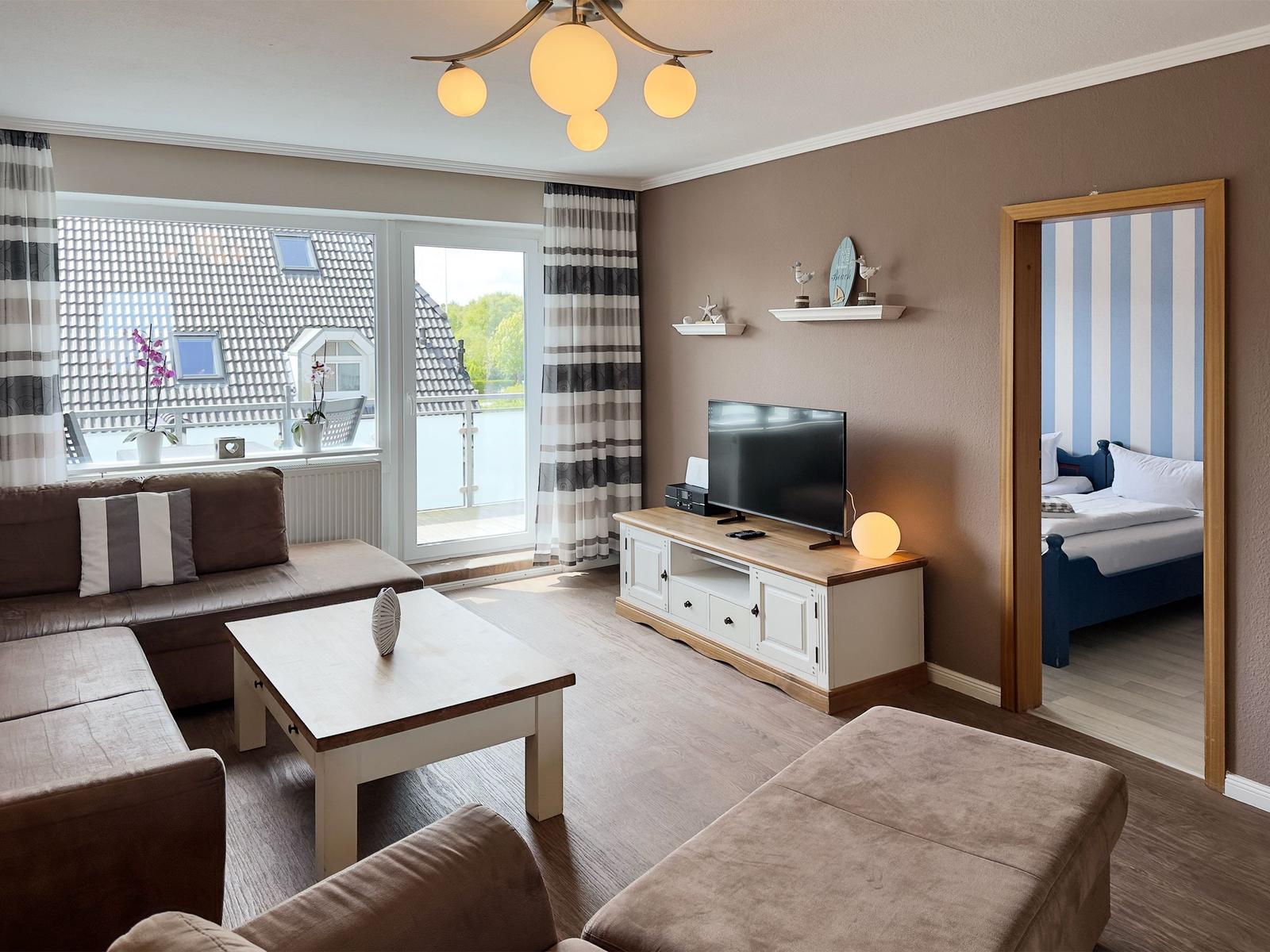 Living room with sofa, TV, and balcony view. Bedroom with bed visible.