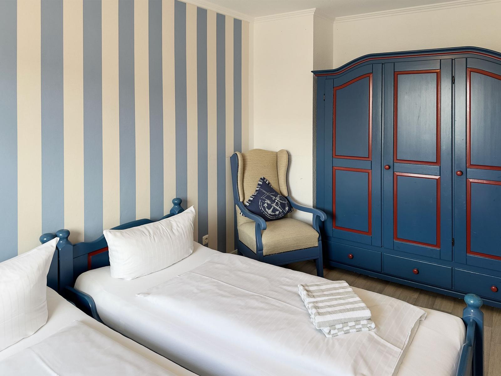 Room with two beds, blue wardrobe, and striped wall wallpaper.