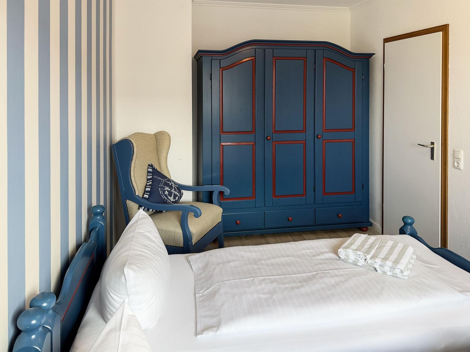 Bedroom with bed, chair, and wardrobe. Wall with stripe pattern.