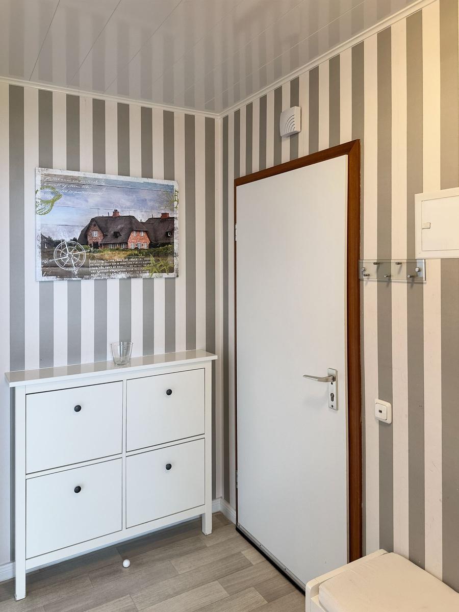 Room with striped wall, white door, and cabinet with picture.