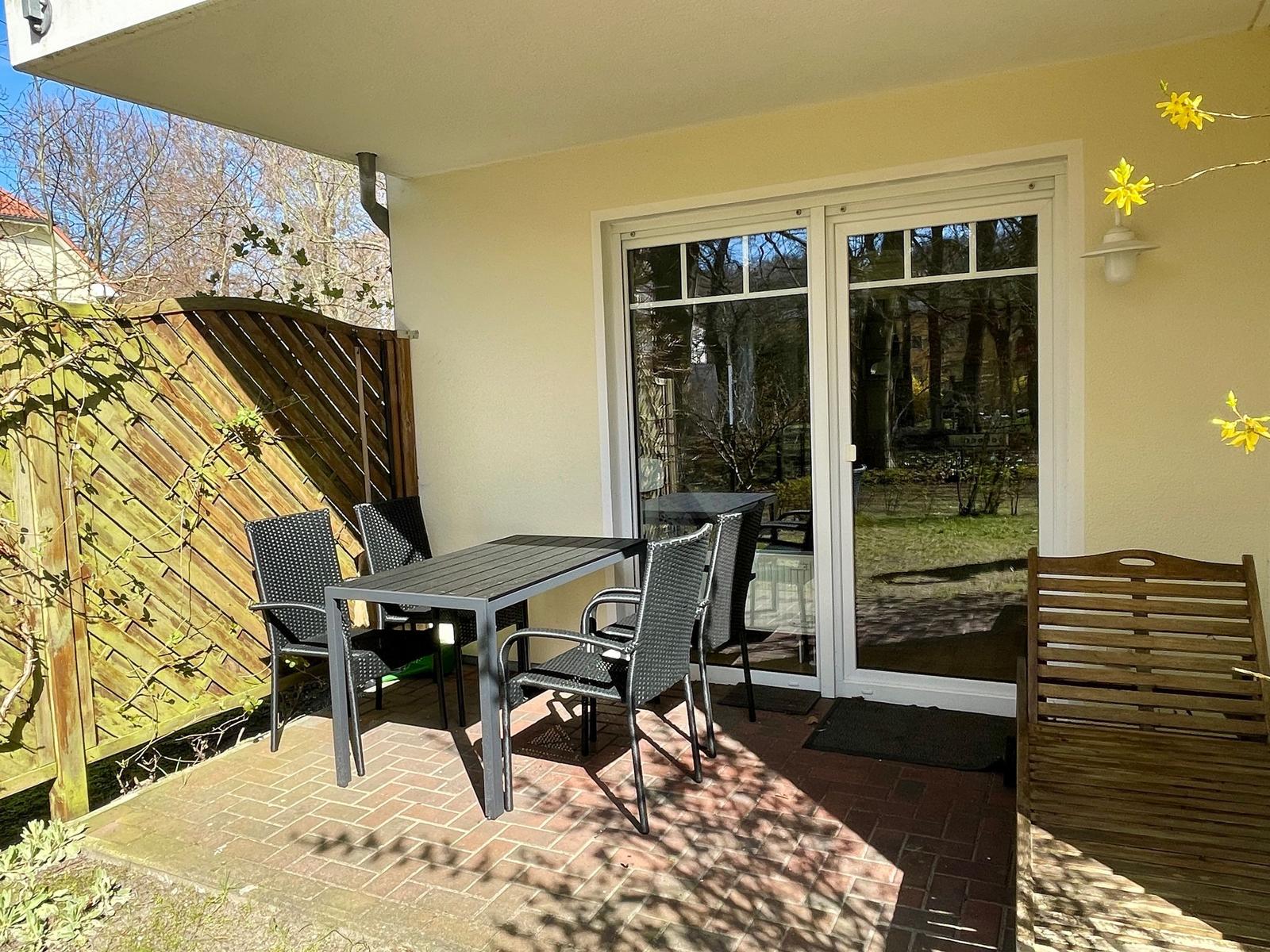 Terrasse mit Tisch, Stühlen und Holzbank. Durch Glastür Zugang zum Innenraum.
