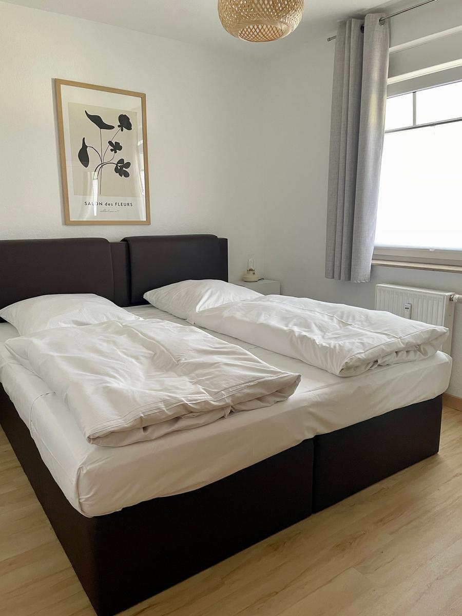 Schlafzimmer mit Doppelbett, Fenster und Wandbild.