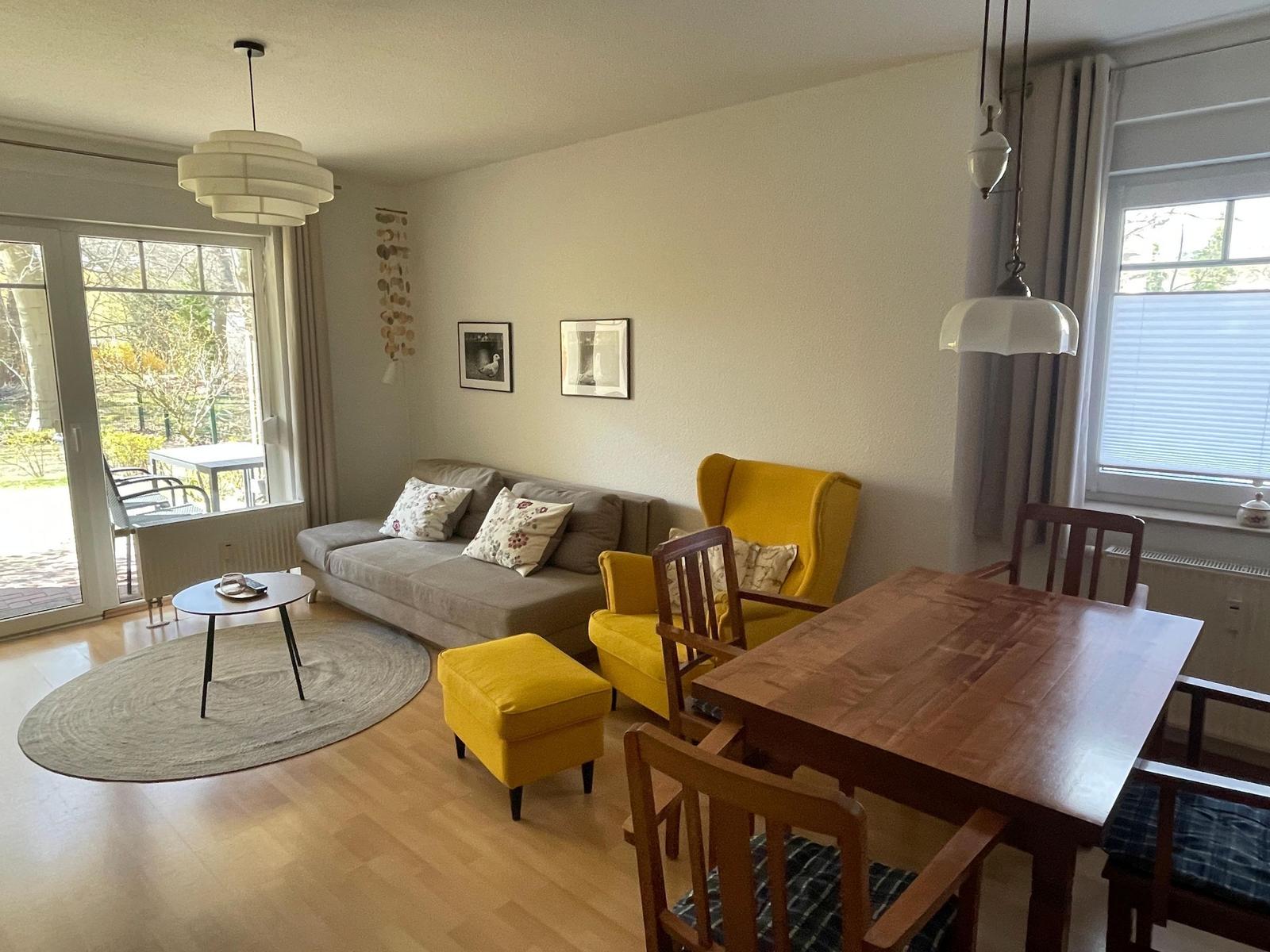 Wohn- und Essbereich mit Sofa, gelber Sessel und Holztisch.
