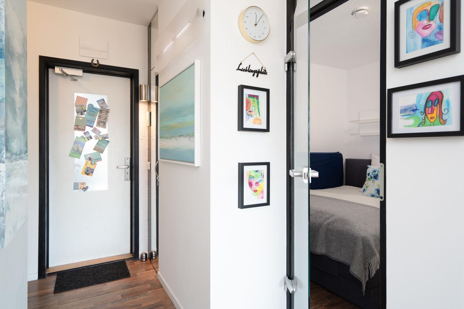 Entryway with door, wall art, and view into bedroom with bed.