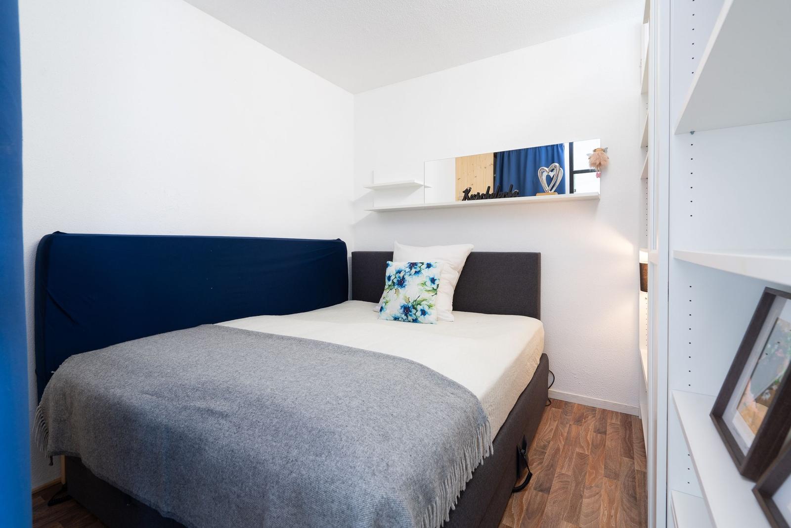Bedroom with bed, pillows, and closet. Wall mirror and wooden floor.